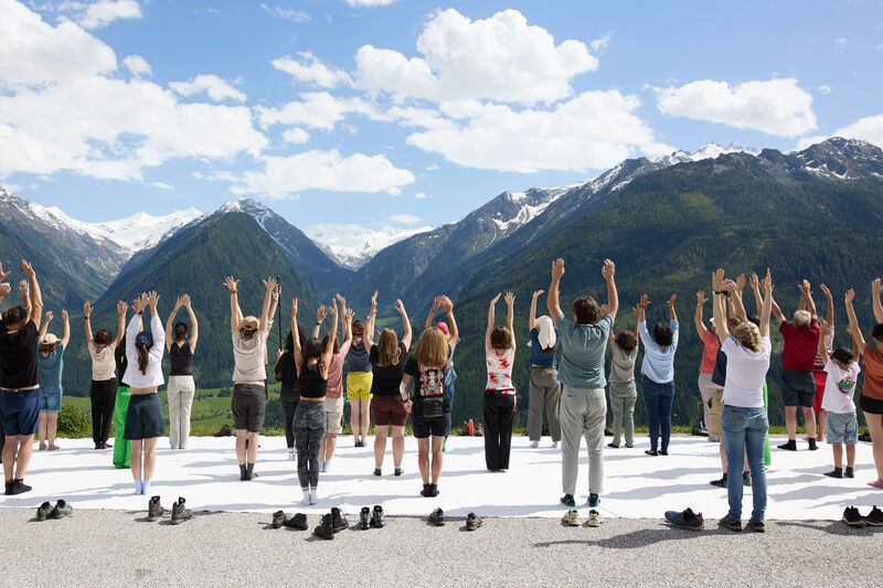 Die Gruppe steht auf einem weissen Tuch, alle heben die Arme in die Luft, im Hintergrund die Berge